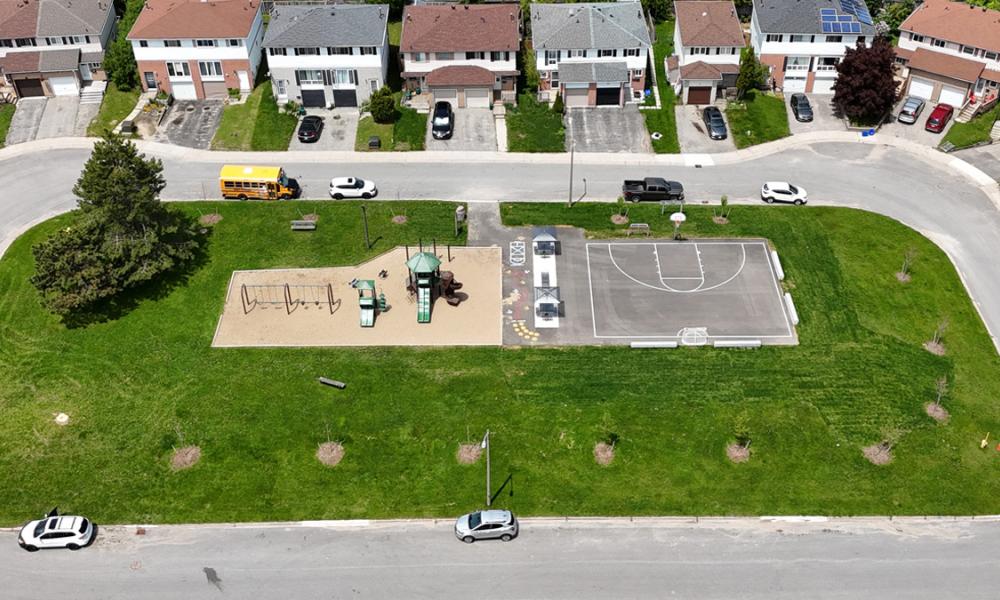 aerial view of park with a playground and basketball court, and street with houses