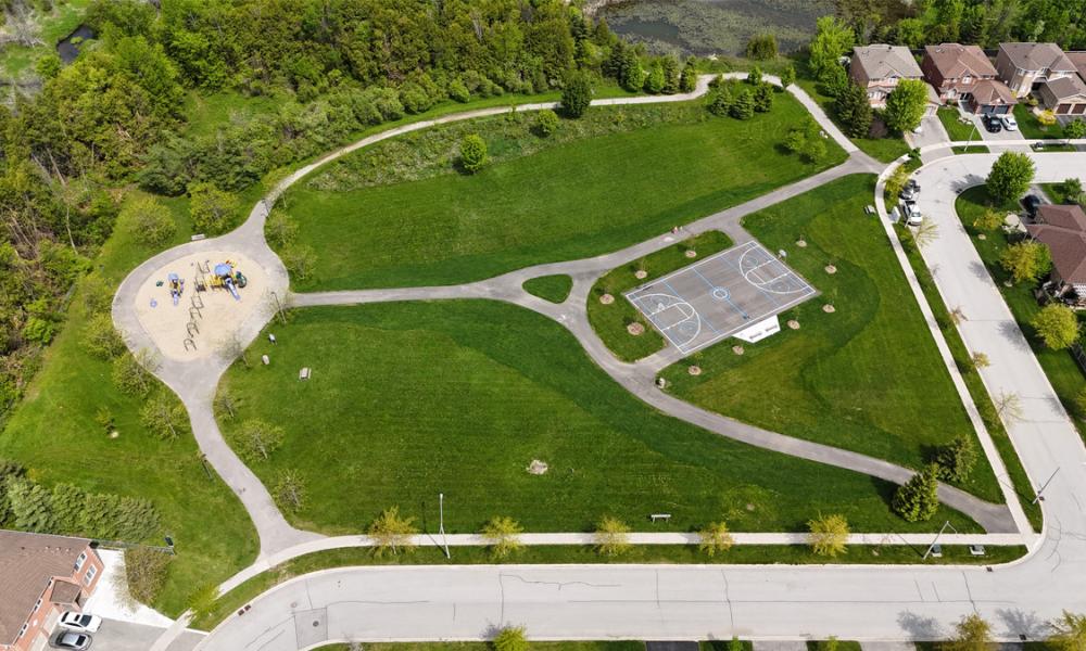 Aerial view of park with playground, sports court and green space, surrounded by trees and houses