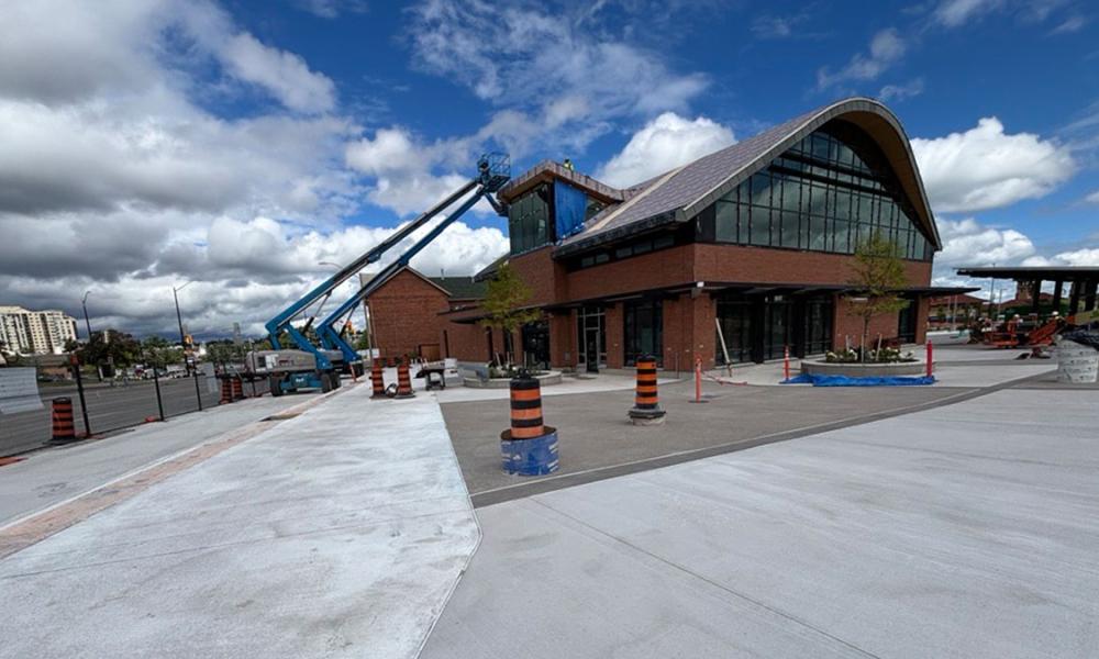 Exterior view of the Barrie Allandale Transit under construction, featuring its distinctive arched roof, with construction work and machinery visible.