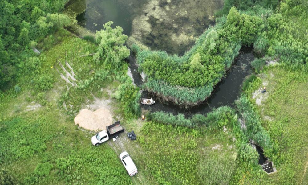 Aerial view of a meandering river surrounded by lush greenery with several vehicles parked nearby on a patch of dirt.