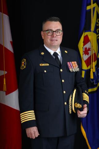 A man in a formal firefighter uniform stands with flags in the background.
